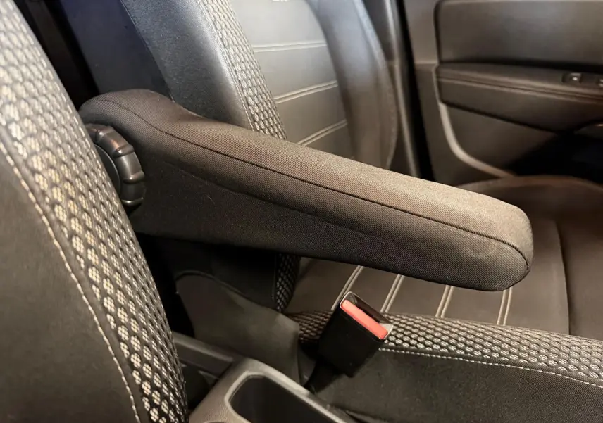 Accoudoir central relevé entre les sièges avant en tissu noir du Dacia Duster, détail intérieur.