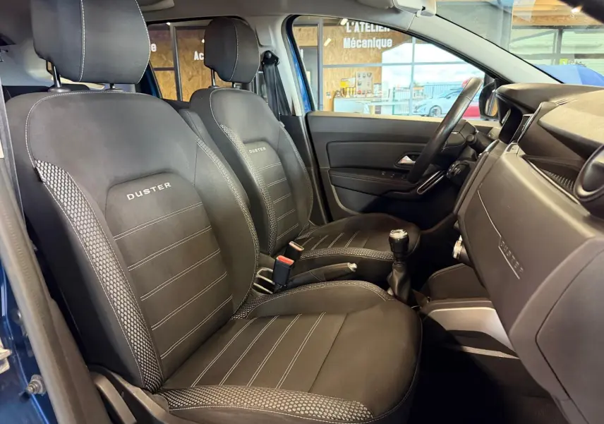Intérieur du Dacia Duster bleu, vue côté droit sur sièges tissu Prestige noirs avec logo Duster brodé.