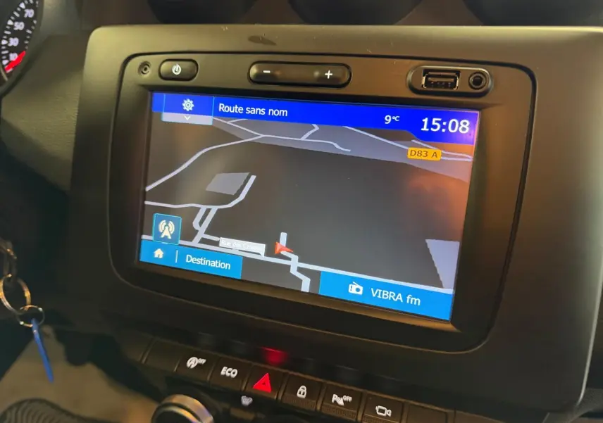 Écran tactile du GPS allumé dans le tableau de bord noir du Dacia Duster bleu, avec commandes climatisation et mode Eco visibles.