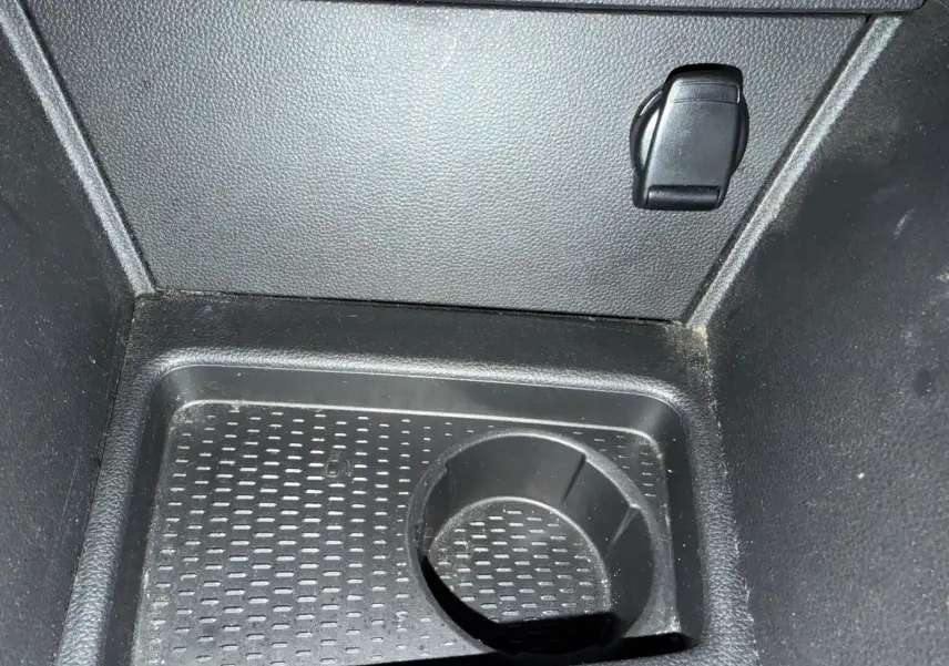 Prise 12V et rangement intérieur en plastique noir du coffre du Dacia Duster bleu, vue rapprochée du plancher.