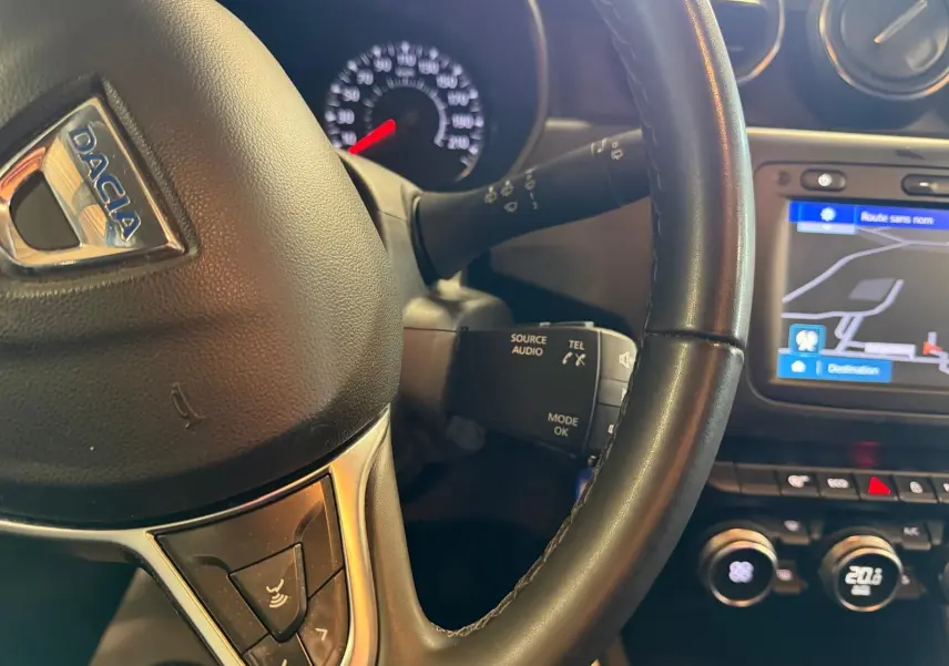 Gros plan sur le volant noir du Dacia Duster avec commandes audio et écran de navigation affichant une carte.