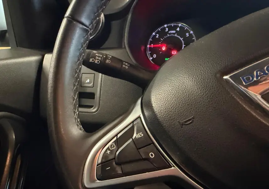 Gros plan sur le volant noir du Dacia Duster bleu, avec commandes intégrées et tableau de bord éclairé en arrière-plan.