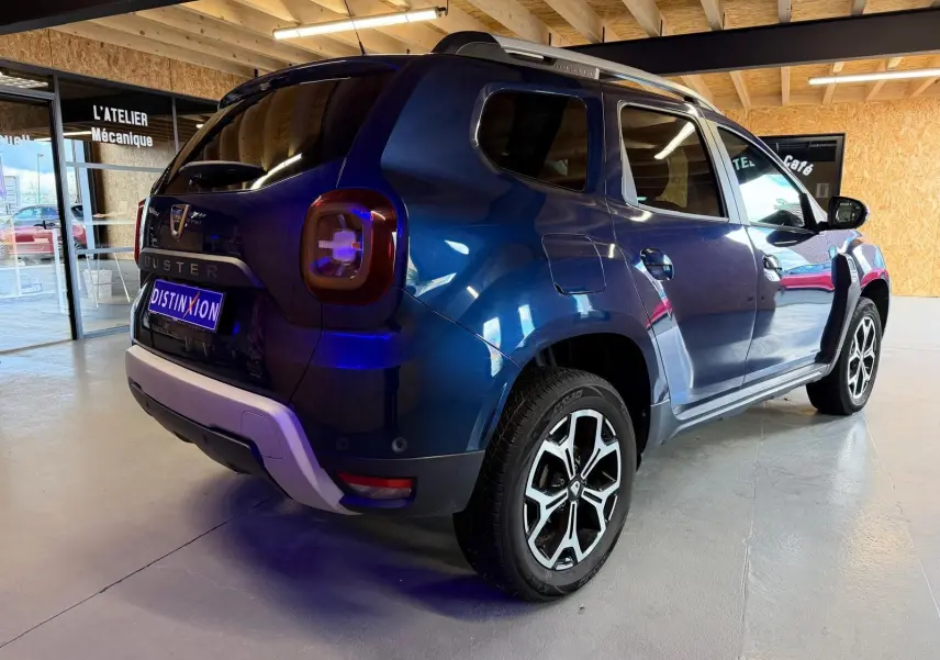 Vue 3/4 arrière droite d'un Dacia Duster bleu avec jantes alliage 17'' Maldives et bouclier arrière ton carrosserie.