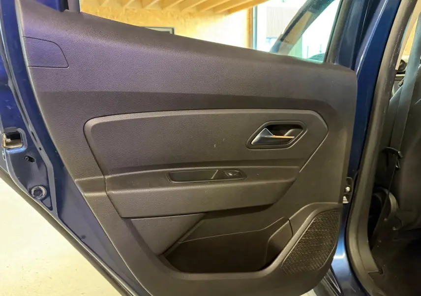 Gros plan sur la porte arrière gauche noire du Dacia Duster bleu, avec poignée et commande de vitre visible.