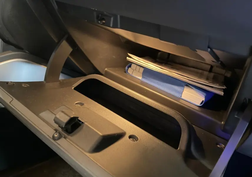 Gros plan sur la boîte à gants ouverte du Dacia Duster bleu, montrant des documents et un manuel rangés à l'intérieur.