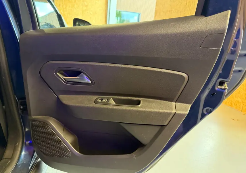 Vue côté gauche de la porte avant bleue du Dacia Duster, avec poignée intérieure et commande de vitre électrique.