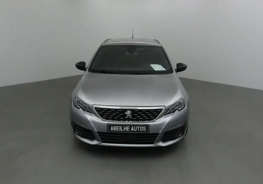 Peugeot 308 SW gris Artense vue de face dans un studio, calandre et logo lion bien visibles.