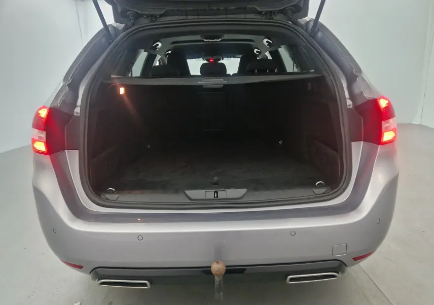 Vue arrière ouverte de la Peugeot 308 SW gris Artense, coffre spacieux avec feux arrière allumés et attelage visible.