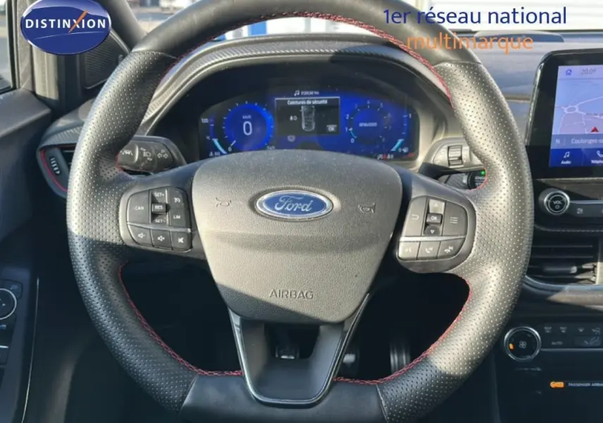 Vue centrée sur le volant perforé avec surpiqûres rouges du Ford Puma gris foncé, tableau de bord numérique et écran tactile visibles.