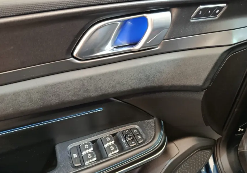 Détail de la porte côté conducteur du LINK & CO 01 bleu, avec poignée alu, surpiqûres bleues et commandes des vitres.