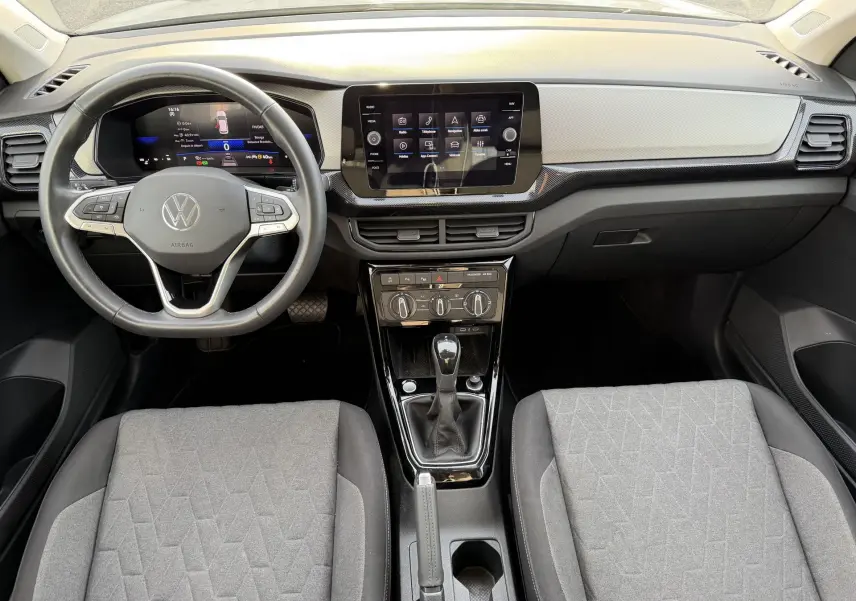 Vue intérieure avant du Volkswagen T-Cross 2025 avec tableau de bord gris, volant multifonction et écran tactile central.