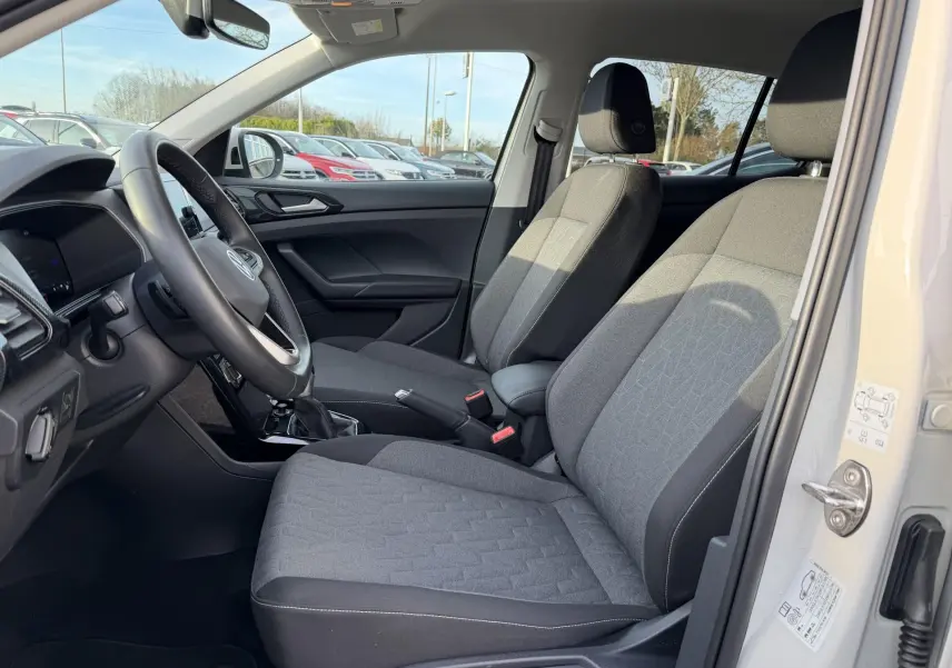 Vue intérieure côté conducteur du Volkswagen T-Cross 2025, sièges tissu gris et volant multifonction cuir.