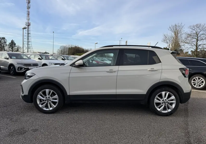 Vue de profil droit d'un Volkswagen T-Cross gris clair avec jantes alliage et toit noir sur parking extérieur.