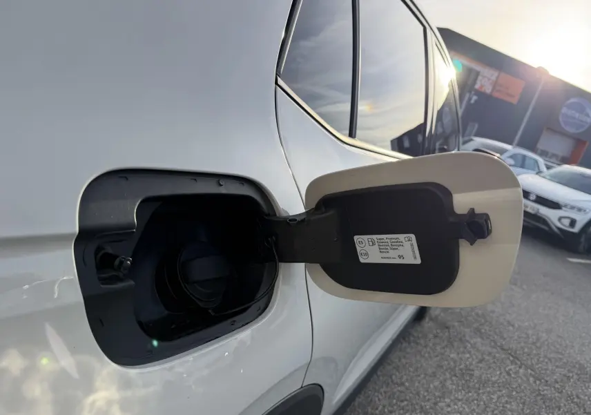 Gros plan sur la trappe à carburant ouverte côté gauche d'un Volkswagen T-Cross gris sous lumière naturelle.