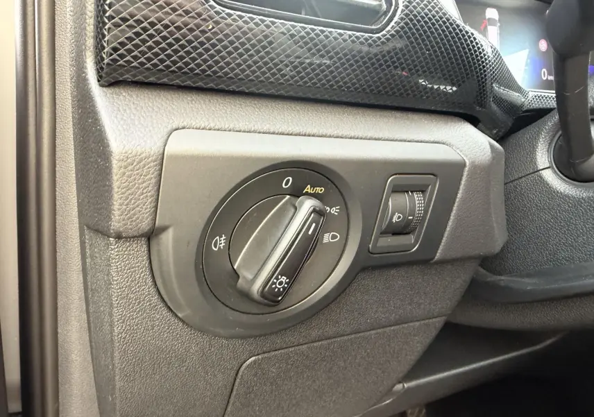 Gros plan sur la commande des phares du tableau de bord d’un Volkswagen T-Cross gris, côté gauche du volant.