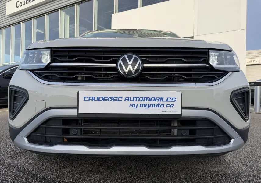 Vue frontale rapprochée du Volkswagen T-Cross gris avec calandre noire et logo VW central bien visible.