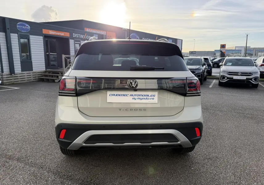 Vue arrière d'un Volkswagen T-Cross gris clair avec feux arrière LED et logo VW central sur un parking.