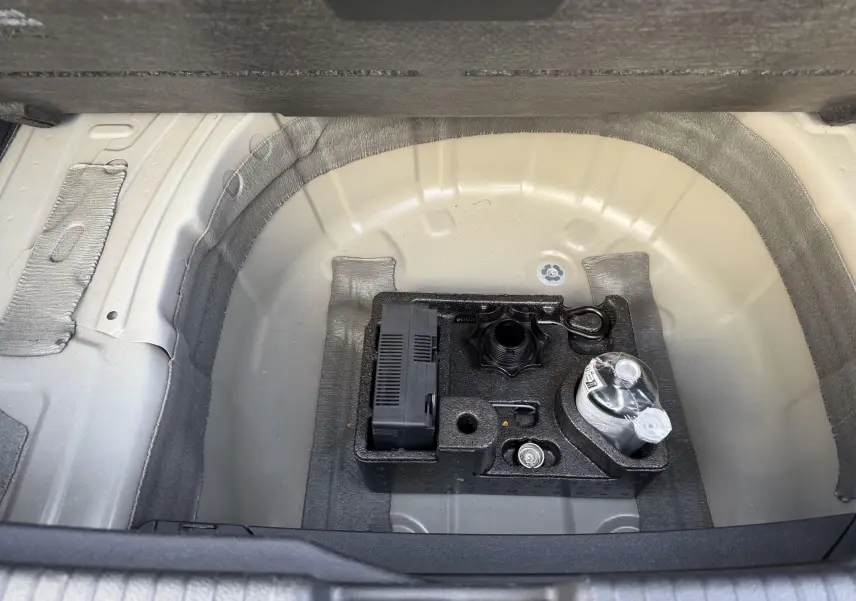 Vue plongeante sur le coffre ouvert d'un Volkswagen T-Cross gris, montrant le kit de dépannage sous le plancher.