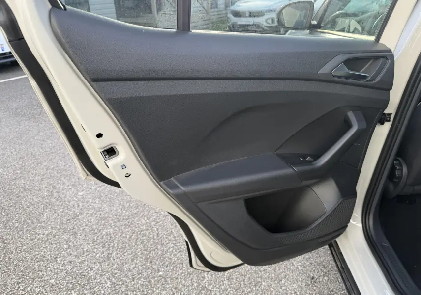 Vue intérieure de la porte arrière gauche noire du Volkswagen T-Cross 2025, avec poignée et commande de vitre visible.