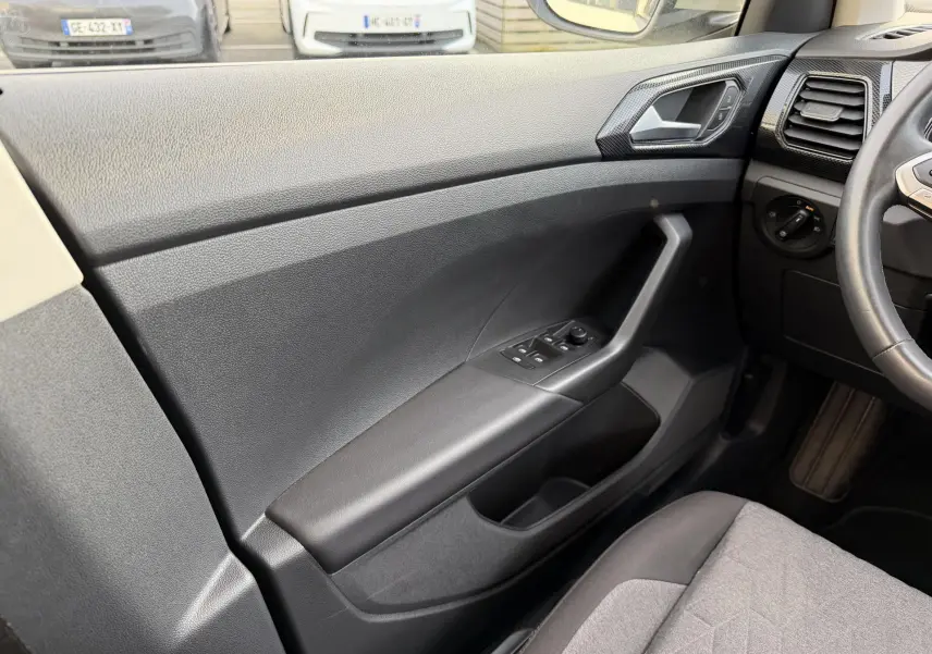 Vue intérieure côté gauche de la porte avant du Volkswagen T-Cross 2025 avec commandes de vitres et accoudoir noir.