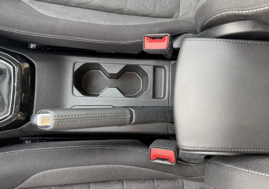 Vue plongeante sur la console centrale noire du Volkswagen T-Cross avec frein à main manuel et porte-gobelets.