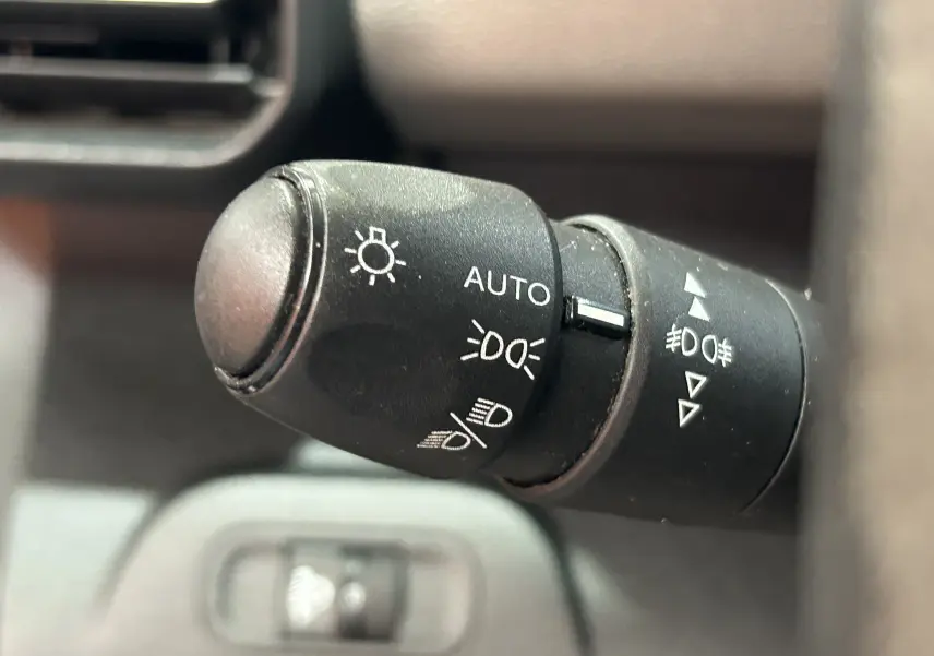 Gros plan sur la commande des feux du Peugeot Rifter gris sable, montrant les réglages automatiques et manuels.