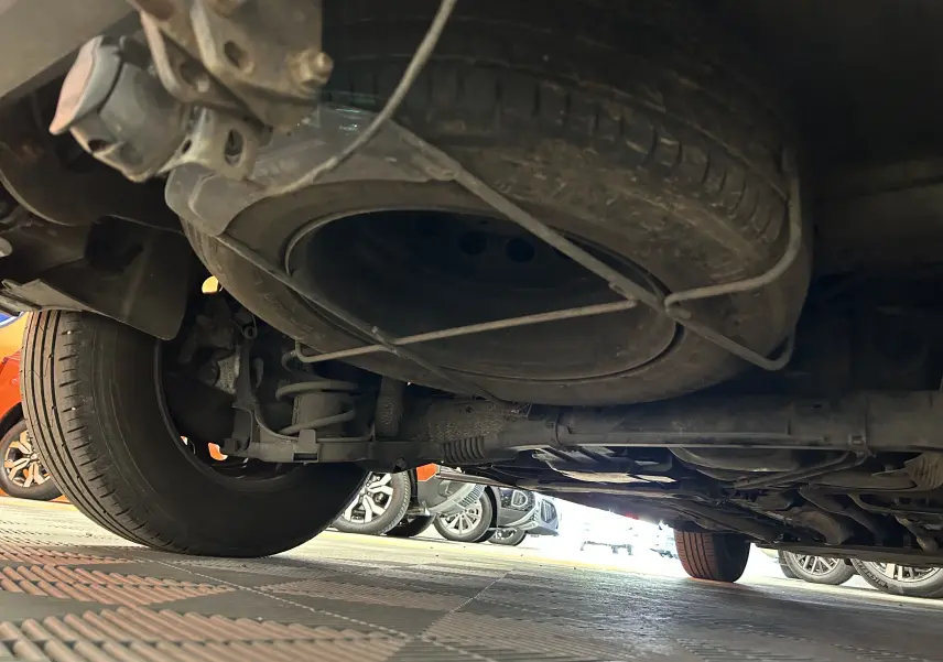 Vue en contre-plongée sous le PEUGEOT RIFTER gris sable, montrant la roue de secours et le train arrière.