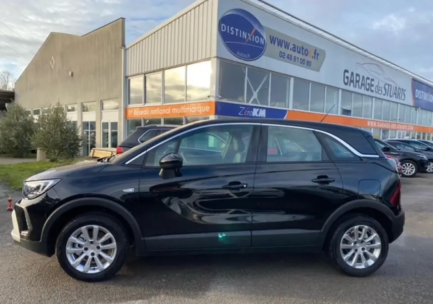 Opel Crossland noir métal vue de profil côté gauche, stationné devant un garage avec vitres teintées et jantes argentées.
