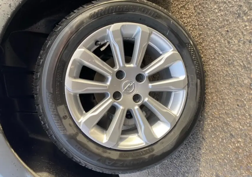 Gros plan sur la roue de secours avec jante alliage argentée et logo Opel au centre, sur fond noir métallisé.