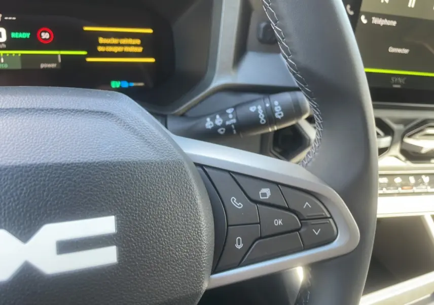 Gros plan sur le volant cuir de la DACIA BIGSTER Hybrid 155 Journey City avec commandes multifonctions et tableau de bord digital.