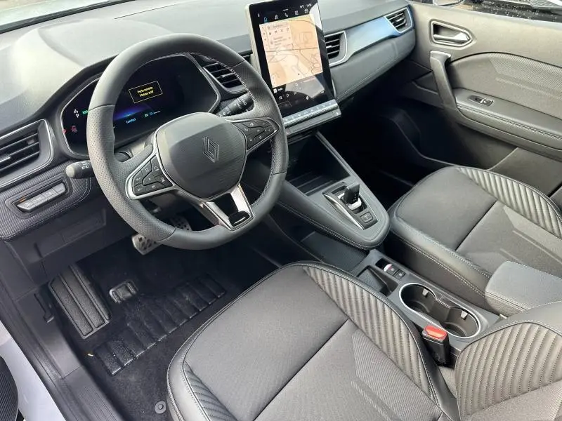 Vue intérieure côté conducteur du Renault Captur 2026 hybride, avec volant multifonction, écran tactile vertical et sellerie noire à motifs.