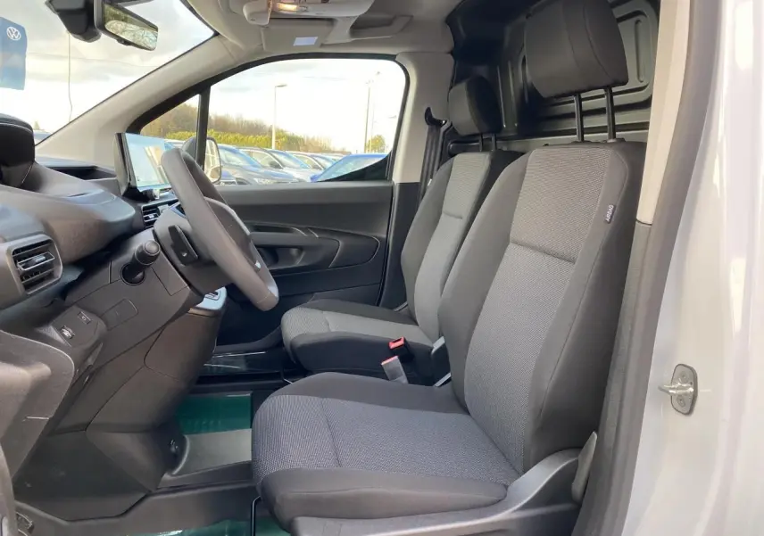 Vue intérieure côté conducteur du Peugeot Partner Fourgon blanc 2025, sièges tissu gris et tableau de bord moderne.