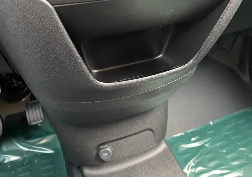 Gros plan sur la console centrale noire du Peugeot Partner Fourgon 2025 avec prise 12V et tapis de protection vert.