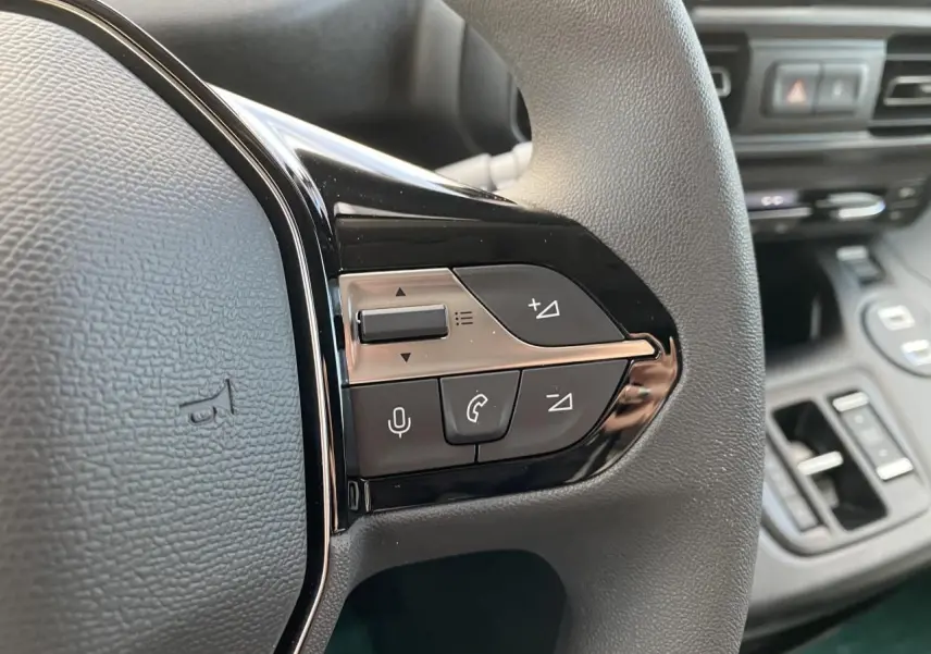 Gros plan sur les commandes multifonctions à droite du volant noir du Peugeot Partner Fourgon blanc, avec tableau de bord flou en arrière-plan.