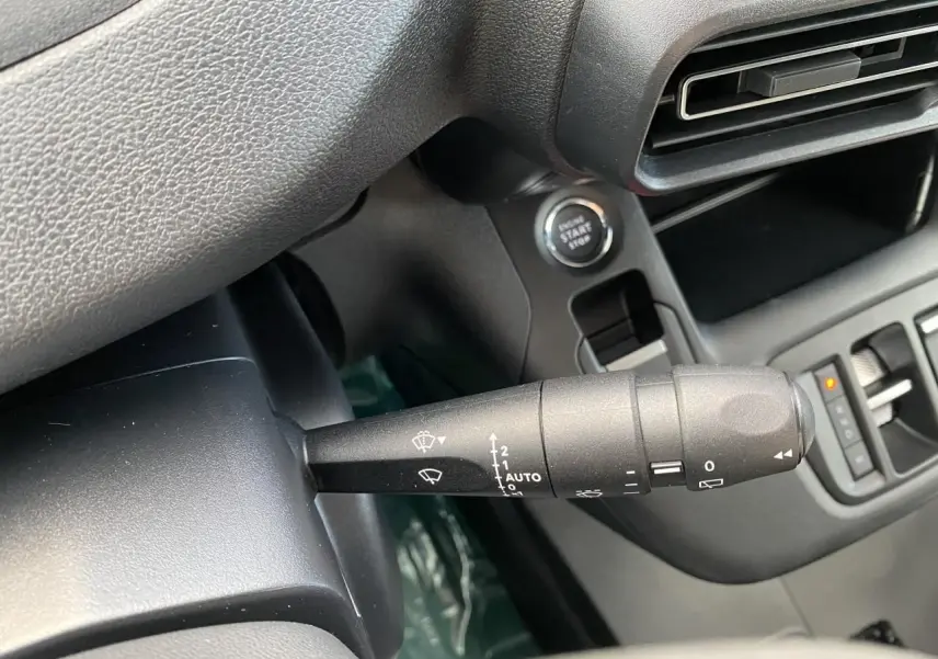 Gros plan sur la commande d’essuie-glace à gauche du volant dans l’habitacle noir du Peugeot Partner Fourgon blanc.