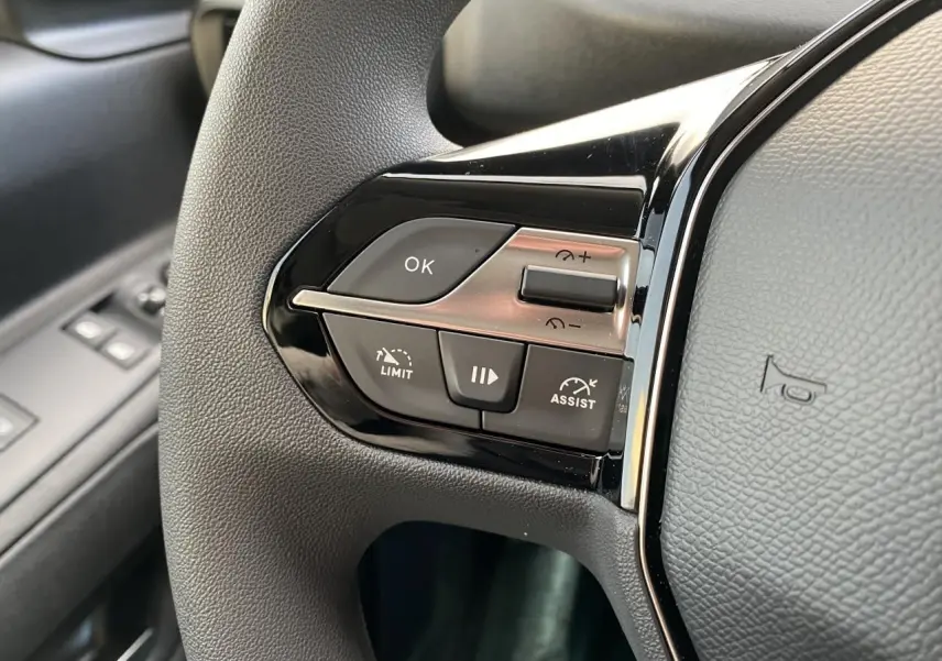 Gros plan sur les commandes de régulateur de vitesse au volant noir du Peugeot Partner Fourgon blanc, côté conducteur.