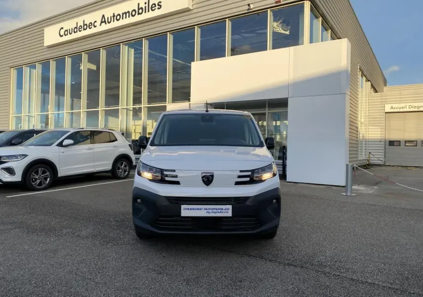 Vue de face du Peugeot Partner Fourgon blanc stationné devant un concessionnaire avec calandre noire et phares allumés.
