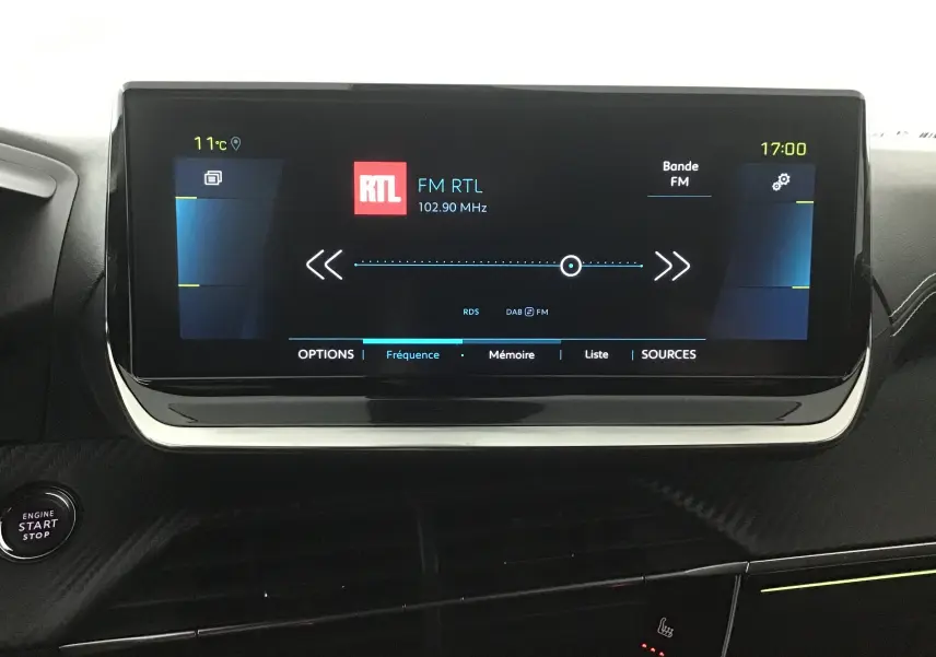 Écran tactile central du tableau de bord du Peugeot 2008 électrique gris, affichant la radio FM RTL à 17h00.