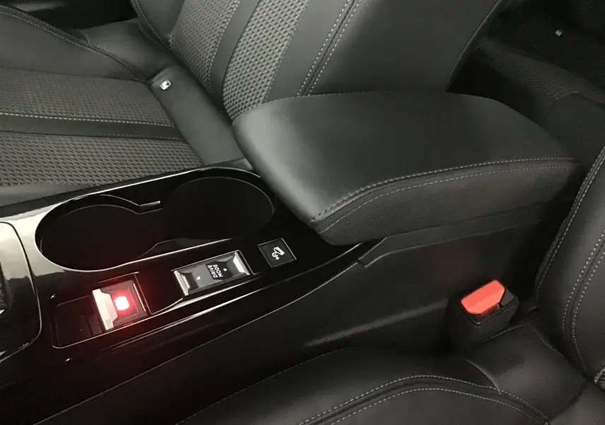 Gros plan intérieur sur la console centrale noire avec accoudoir cuir et bouton Drive Mode du Peugeot 2008 électrique gris Artense.
