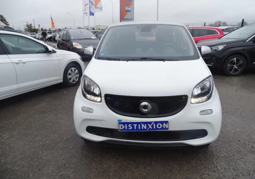 Vue de face d'une Smart Forfour électrique blanche avec calandre noir brillant et feux allumés sur parking.