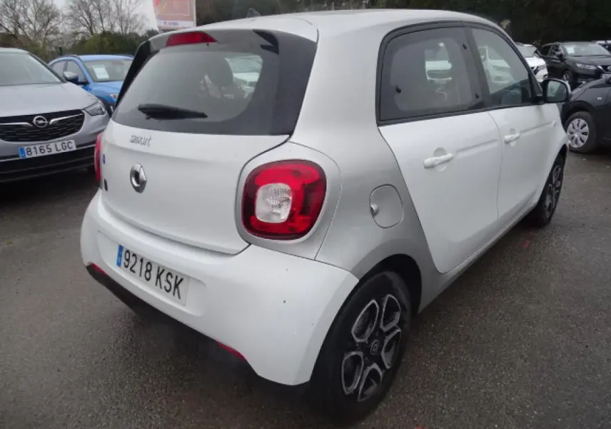 Vue 3/4 arrière droite d'une Smart Forfour électrique blanche avec jantes alliage bicolores et logo smart EQ visible.