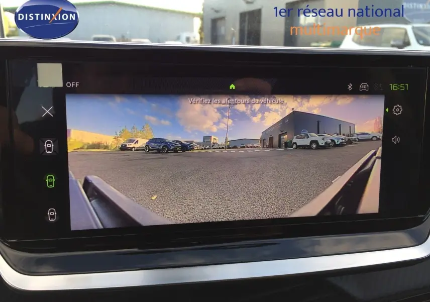 Vue de la caméra de recul du Peugeot 208 gris Artense, affichant le parking et plusieurs véhicules en arrière-plan.