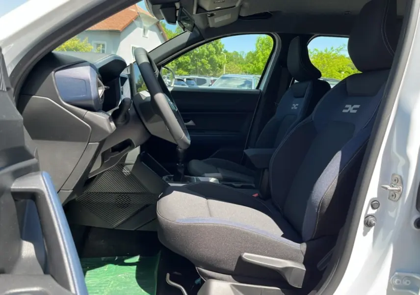 Intérieur du DACIA BIGSTER blanc glacier, vue côté gauche sur les sièges avant avec logo brodé et volant multifonction.
