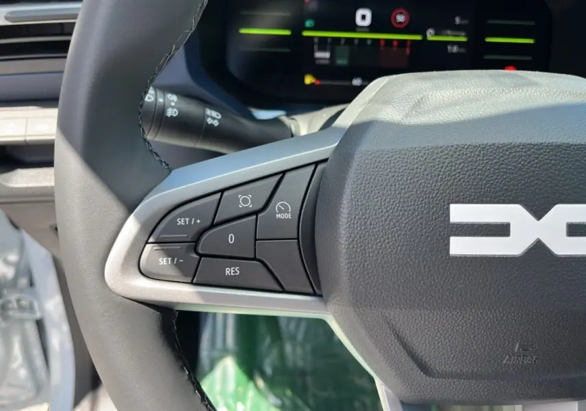 Gros plan sur le volant cuir du Dacia Bigster 2025 blanc glacier, avec commandes multifonctions et tableau de bord numérique.