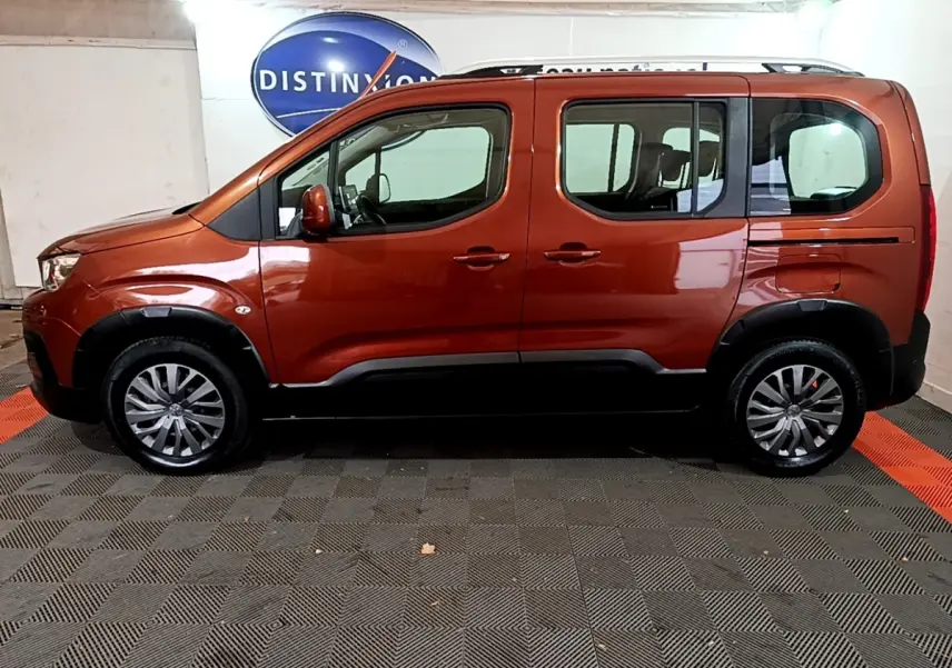 Profil côté gauche d'un Peugeot Rifter marron 2019 avec barres de toit chromées et jantes alliage en intérieur showroom.