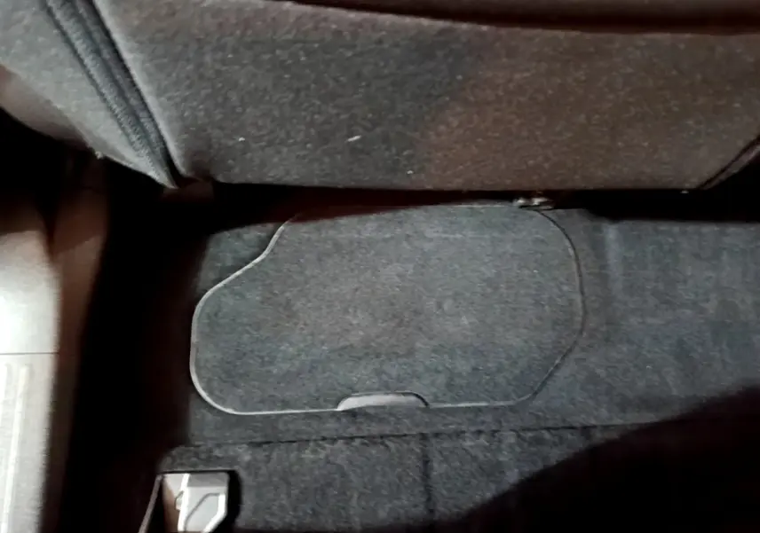 Gros plan sur le rangement sous le siège passager du Peugeot Rifter marron, moquette noire visible.