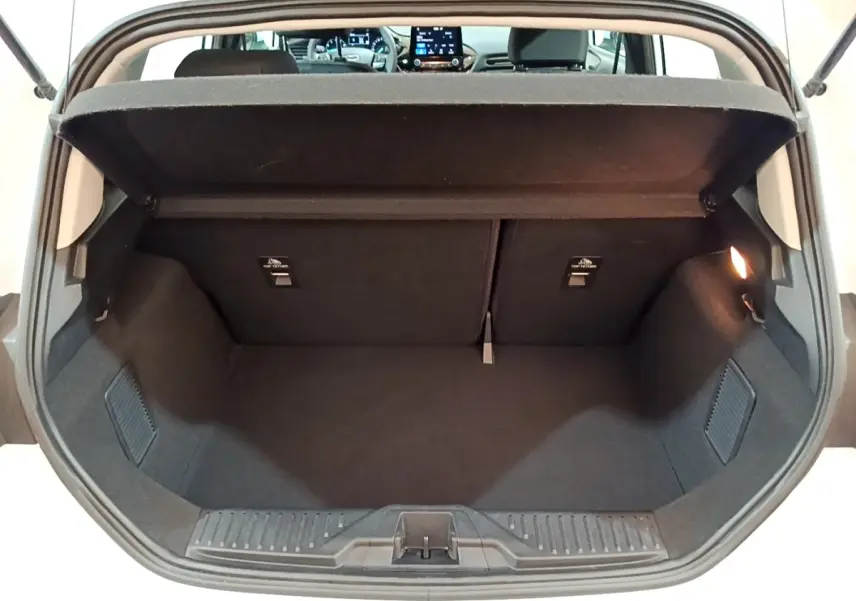 Coffre ouvert vu de l'arrière d'une Ford Fiesta blanche 2022, intérieur noir et tablette de coffre relevée.