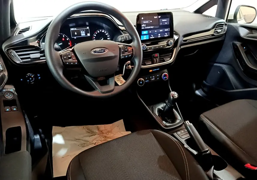 Vue intérieure avant de la Ford Fiesta blanche 2022, tableau de bord avec écran tactile et volant multifonctions.