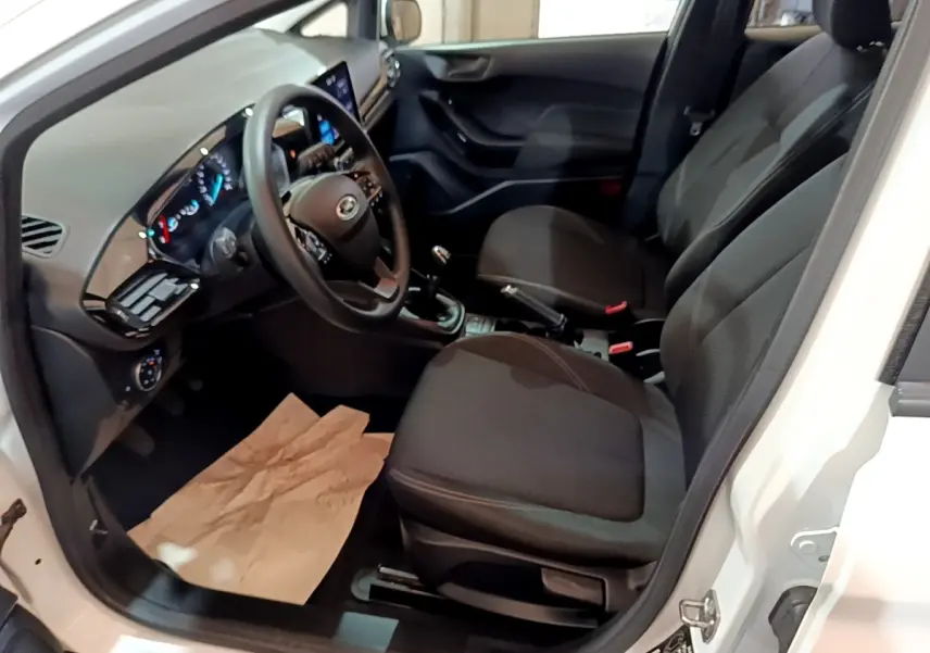 Vue intérieure côté conducteur de la Ford Fiesta blanche 2022, montrant sièges noirs et tableau de bord digital.