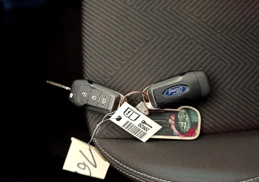 Gros plan sur deux clés Ford posées sur un siège tissu gris foncé avec motifs géométriques.